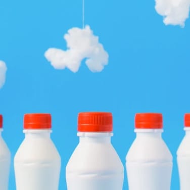 Five aligned milk bottles with red cap with a blue sky background with clouds