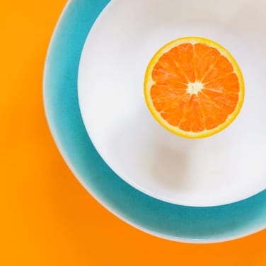 An orange table with a white and blue dish and on the top is an orange.